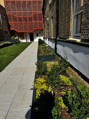 A pathway leading to a building with a brick facade and a modern orange lattice structure. - Stonehouse Stays · Luxury Clapham 1-Bed. (London)