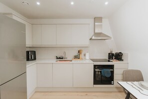 A modern kitchen with white cabinetry, a built-in oven, a coffee machine, and a dishwasher. - Stonehouse Stays · Luxury Clapham 1-Bed. (London)