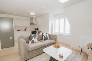 A modern living room with a sofa, a coffee table with fruit, and a view of the kitchen. - Stonehouse Stays · Luxury Clapham 1-Bed. (London)
