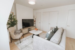 A modern living room with a sofa, a coffee table, a TV, and a small plant. - Stonehouse Stays · Luxury Clapham 1-Bed. (London)