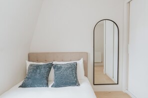 Een slaapkamer met een bed, hoofdeinde, twee kussens en een spiegel.