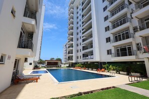 A modern apartment building with a swimming pool, outdoor seating, and a lounge area. - 3-bedroom ocean-view apartment, where modern comfort meets breathtaking views. (Mombasa)