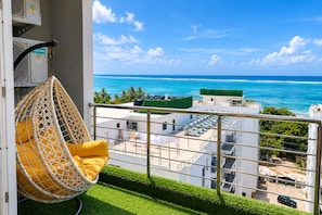 A balcony with a hanging chair, a view of the ocean, and a building with multiple floors. - 3-bedroom ocean-view apartment, where modern comfort meets breathtaking views. (Mombasa)