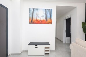 A hallway with a bench, a painting of a forest scene, and a plant. - 3-bedroom ocean-view apartment, where modern comfort meets breathtaking views. (Mombasa)