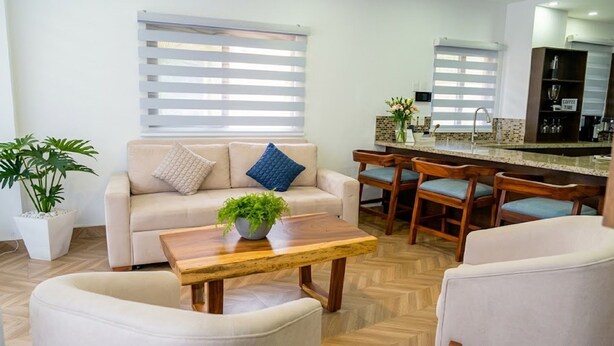 Una sala de estar con sofá, una mesa de centro y una zona de bar con taburetes.