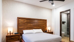Un dormitorio moderno con cabecera de madera, cama con ropa de cama blanca, dos mesitas de noche con lámparas y un mueble auxiliar con un reloj.