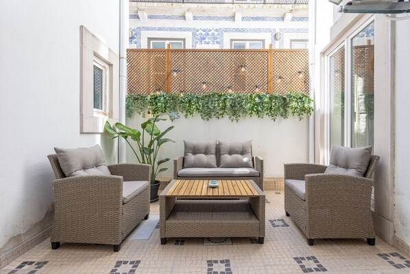 Un patio con mobiliario de mimbre, una planta en maceta y suelo de baldosas.