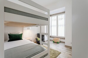 Una cama litera con escritorio y silla, una ventana con cortinas y un pequeño coche de juguete de madera.