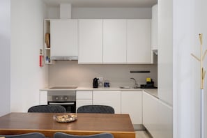 A compact kitchen with white cabinetry, a built-in oven, a coffee maker, and a sink. - Baixa Garden: 2BR + Patio | Perfect for Groups and Families (Lisboa)