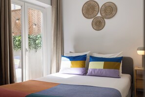 A hotel room with a bed, a nightstand, a lamp, and a view of the outdoors through a sliding door. - Baixa Garden: 2BR + Patio | Perfect for Groups and Families (Lisboa)
