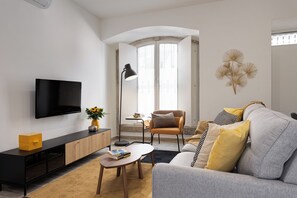 A modern living room with a flat-screen TV, a coffee table, a sofa, and a chair. - Baixa Garden: 2BR + Patio | Perfect for Groups and Families (Lisboa)