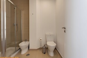 Un baño con cabina de ducha de vidrio, un bidé, un inodoro y un cubo de basura.