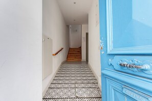 A hallway with patterned floor tiles, a wooden staircase, and a blue door with a decorative handle. - Baixa Garden: 2BR + Patio | Perfect for Groups and Families (Lisboa)