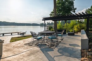 An outdoor patio with a table and chairs, a pergola, and a view of a lake. - Still Waters Lakefront Weddings & Events. Boating, Swimming & Sunset Views (Charlotte)