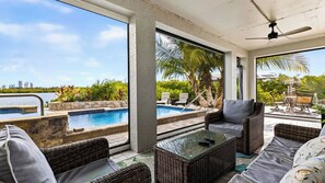 A poolside area with wicker furniture, a glass table, and a view of a city skyline. - Sanctuary Point by Avantstay Waterfront Pool + Spa Kayak + Fishing Dock Near Beaches (Bonita Springs)