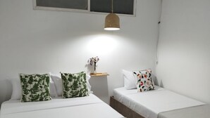 Un dormitorio con dos camas, una mesita de noche con un florero y un ventilador colgante.