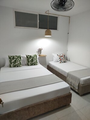 A bedroom with two beds, a bedside table with a vase, and a hanging fan. - Vrbo Property (Cartagena de Indias)