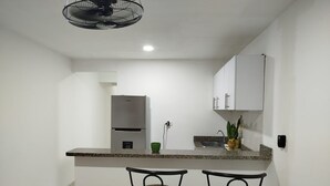 Una cocina compacta con refrigerador, lavamanos y dos taburetes de bar.