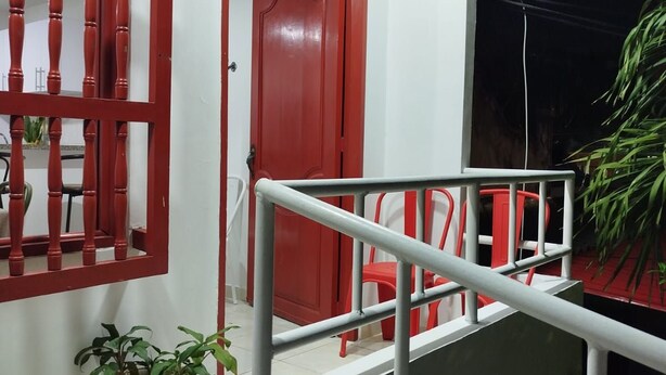 Una escalera con barandilla de metal que lleva a una plataforma, una puerta roja y una planta en maceta en el suelo.