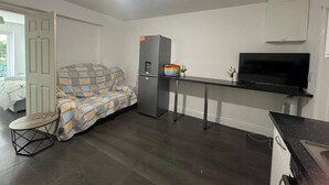 A compact living space with a sofa, a small table, a refrigerator, a TV, and a door leading to an outdoor area. - Apartment Sleeps 7 With Patio (Hayes)