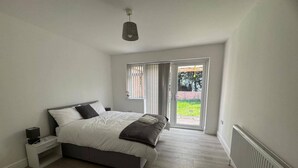 A bedroom with a bed, bedside table, and a view of the outdoors through a sliding door. - Apartment Sleeps 7 With Patio (Hayes)
