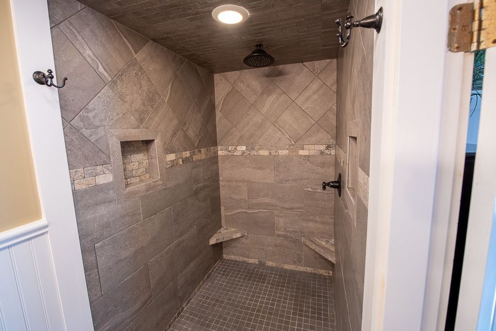 A shower with a tiled wall and a small shelf.