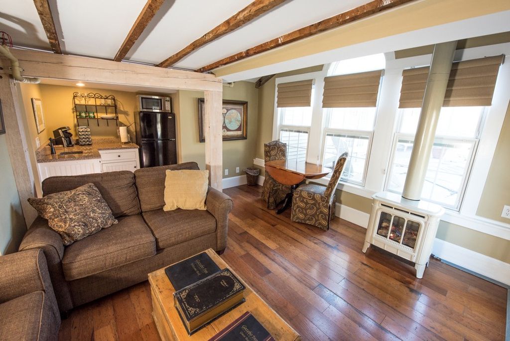 A cozy living room with a sofa, a coffee table with books, a dining area with a table and chairs, and a kitchen with appliances.