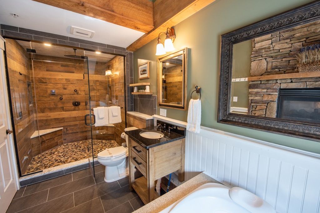 A bathroom with a glass-enclosed shower, a wooden vanity, a white bathtub, and a stone fireplace.