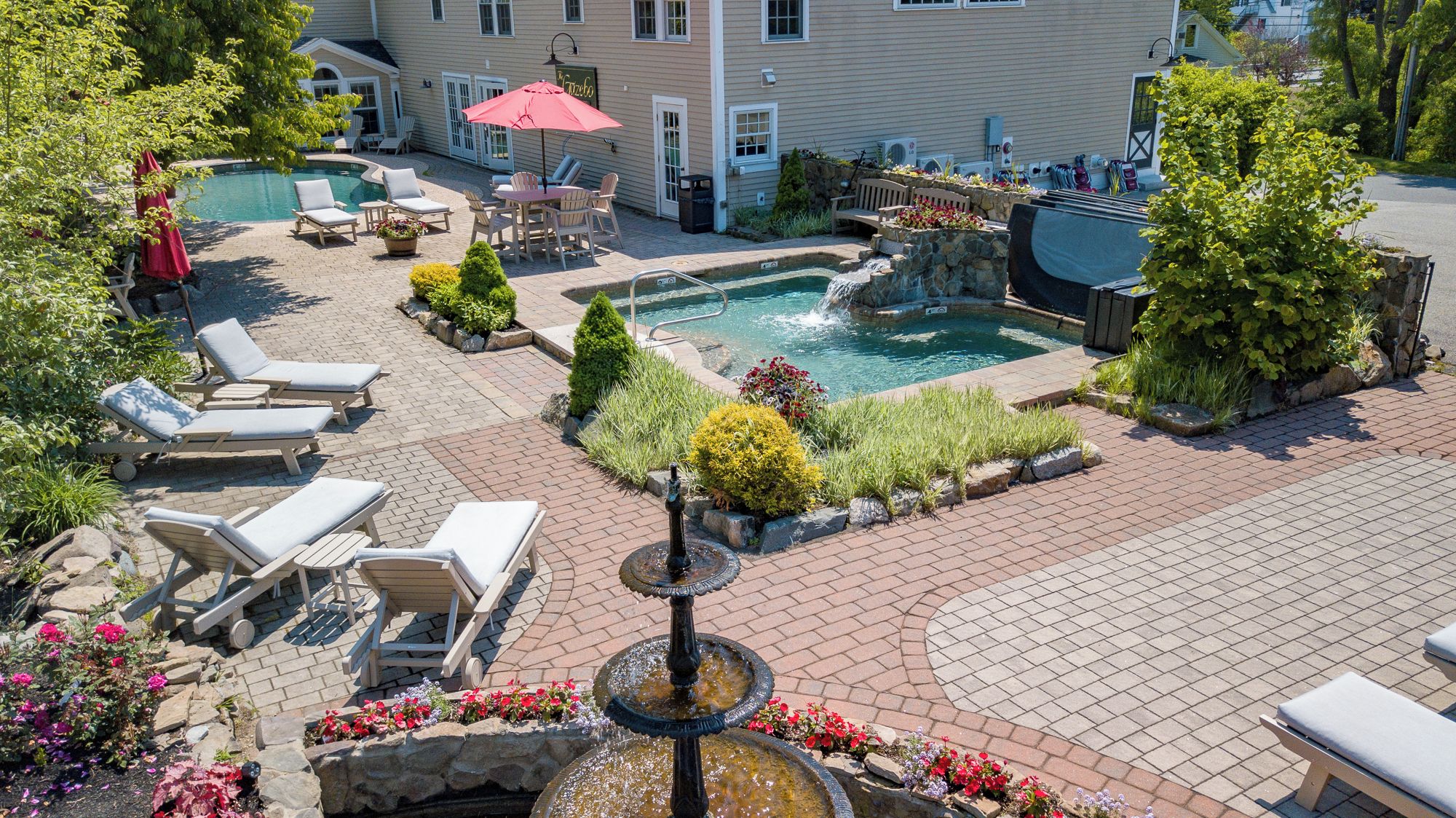 A pool area with lounge chairs, a hot tub, and a fountain.