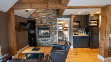 A modern kitchen with dark cabinets, a stone fireplace, and a dining area with leather furniture.