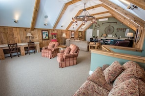 Quarto de sótão com mesa de jantar, duas cadeiras xadrez, um sofá e um banquinho estampado.