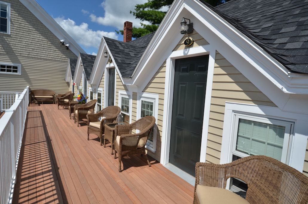 A wooden deck with wicker furniture, a covered area, and a house with a dark roof and beige siding.