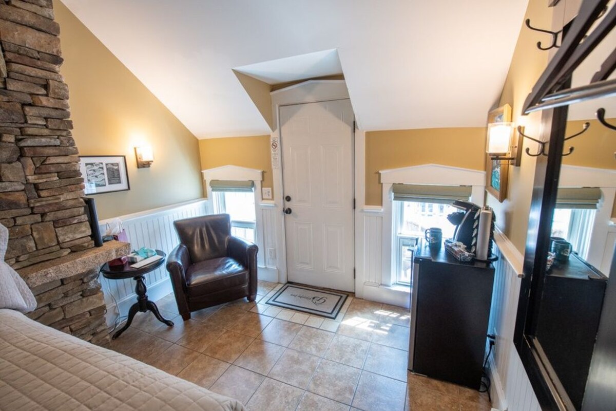 A cozy entryway with a stone wall, a leather chair, a small table, a door, and a refrigerator.