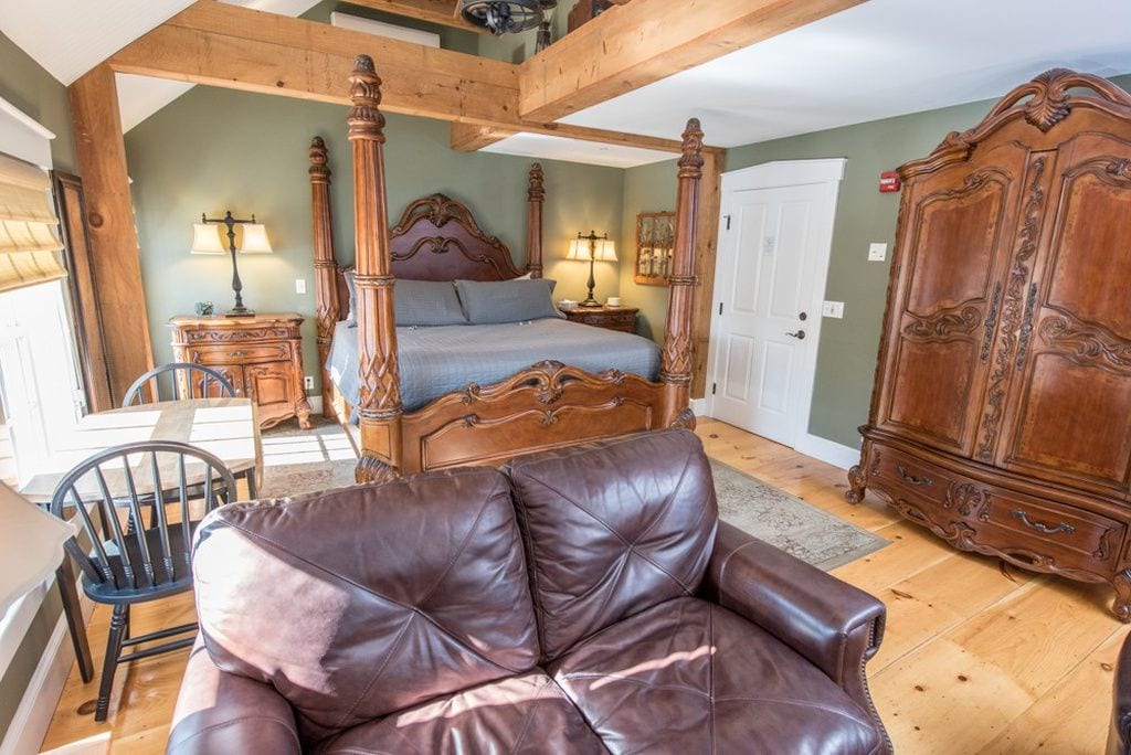 A bedroom with a four-poster bed, a wooden wardrobe, a leather armchair, and a nightstand with lamps.