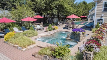 A pool area with lounge chairs, umbrellas, and a hot tub.