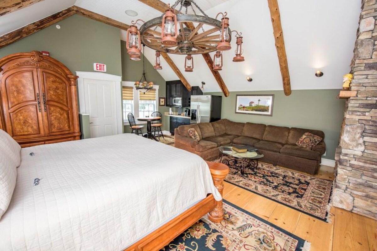 A bedroom with a large bed, a wooden wardrobe, a sofa, and a dining area with a table and chairs.