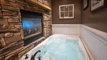 A stone fireplace with a built-in television, a white bathtub with jets, and a framed picture on the wall.