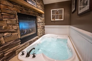 A stone fireplace with a built-in television, a white bathtub with jets, and a framed picture on the wall. - Gazebo Inn (Ogunquit)