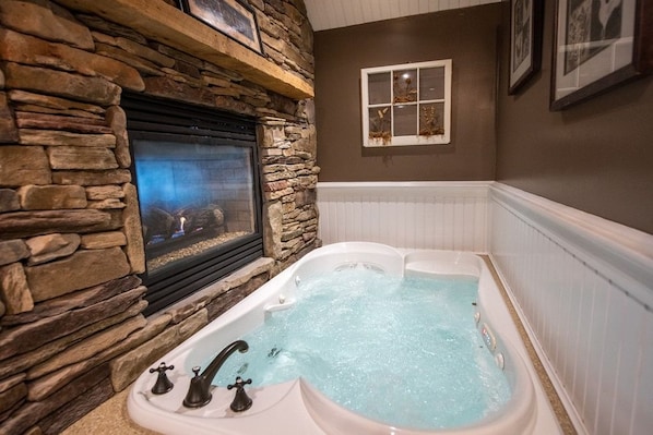 A stone fireplace with a built-in television, a white bathtub with jets, and a framed picture on the wall. - Gazebo Inn (Ogunquit)
