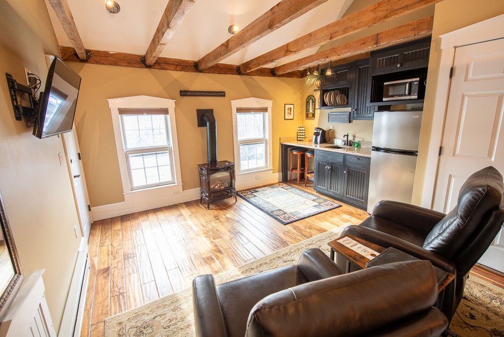 A spacious living area with a fireplace, wooden beams, a flat-screen TV, and a kitchen with modern appliances.
