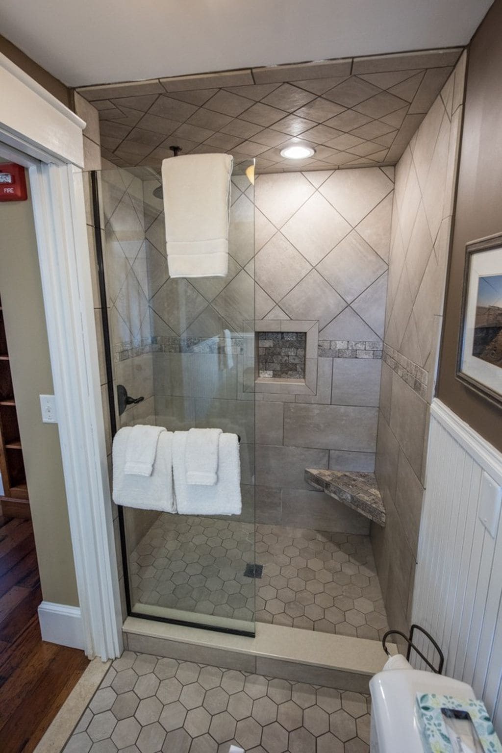 A glass-enclosed shower with a white towel hanging on the door, a tiled floor, and a small stone accent wall.