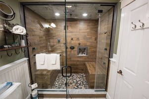 Une douche fermée par des parois de verre, avec un revêtement mural en bois, une serviette blanche et une petite étagère contenant des articles de toilette.