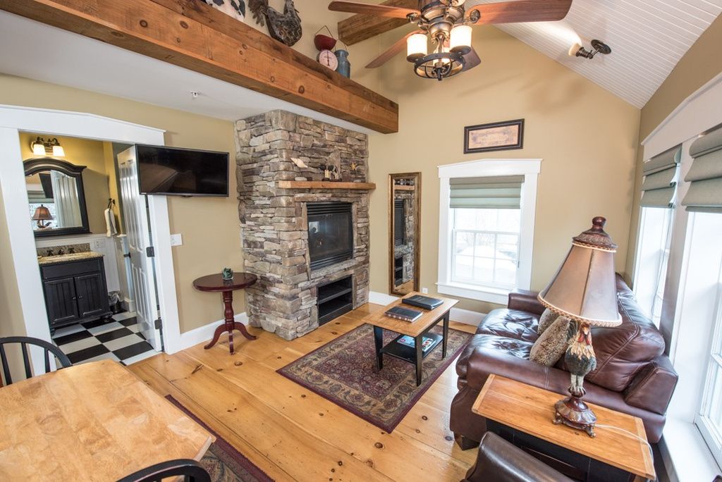 A living room with a stone fireplace, wooden ceiling beams, a television, and a leather sofa.