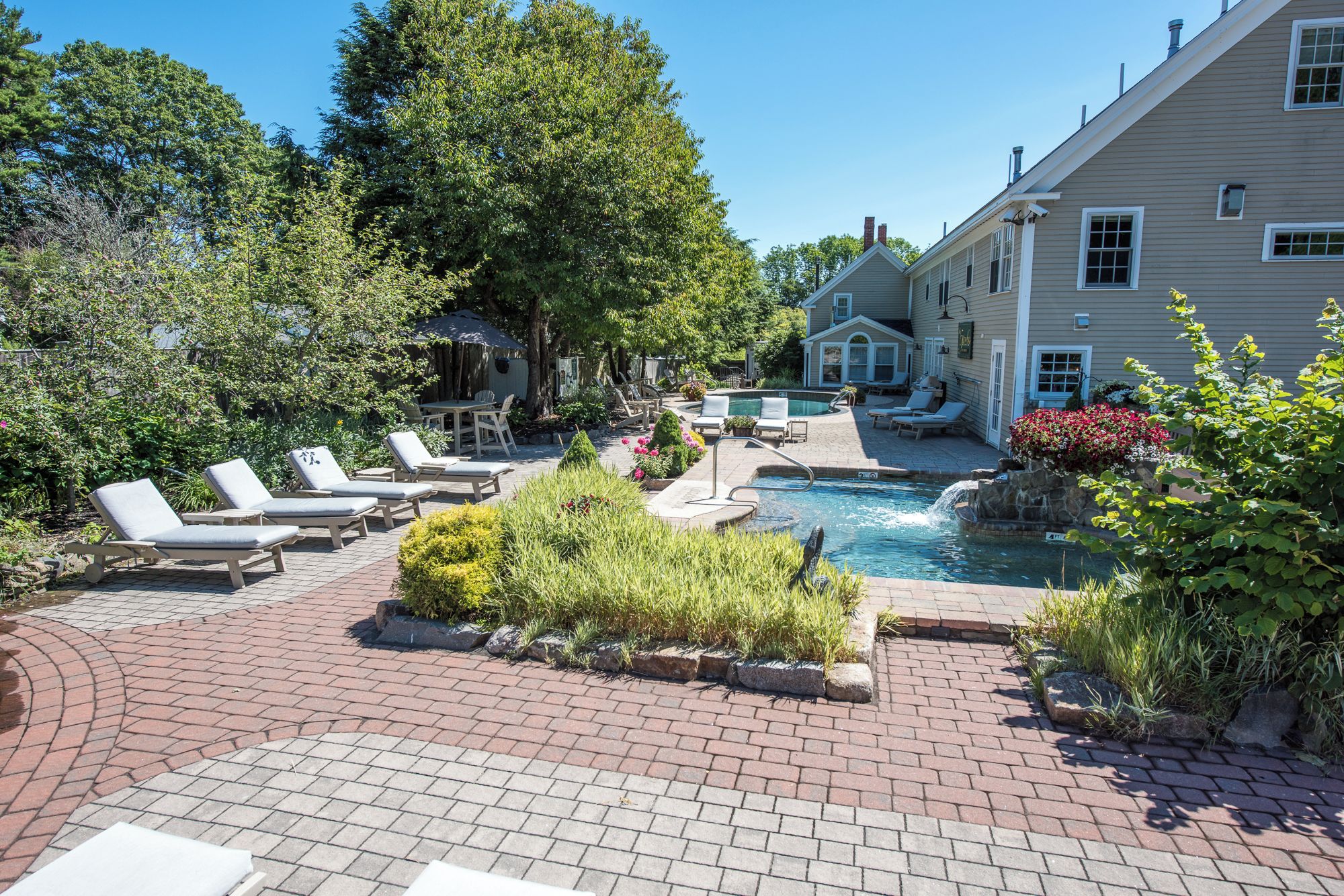 A pool area with lounge chairs, a hot tub, and a brick patio.