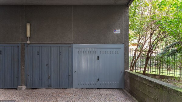 Una entrada protegida por una puerta de metal, un muro de concreto y un área pavimentada con diseño de ladrillo.