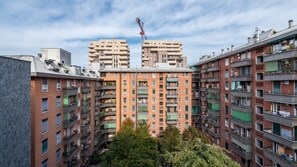 A multi-story residential building with balconies, a crane in the background, and surrounding trees.