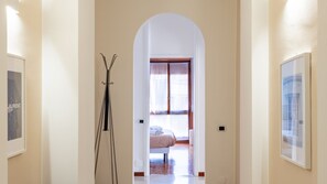 A hallway with an arched doorway leading to a bedroom with a bed and a window.