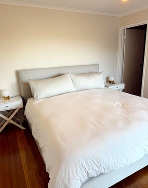 A neatly made bed with a white duvet and pillows, a bedside table with a lamp, and a wooden floor. - Rye Coastal Retreat  (Walk to Tyrone Foreshore) (Rye)