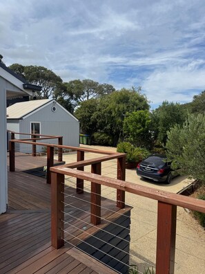 A wooden deck with a metal railing, a car parked in the background, and a building with a white exterior. - Rye Coastal Retreat  (Walk to Tyrone Foreshore) (Rye)