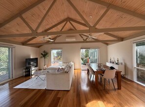 A spacious living area with a high ceiling, wooden beams, a sofa, a dining table, and a television. - Rye Coastal Retreat  (Walk to Tyrone Foreshore) (Rye)